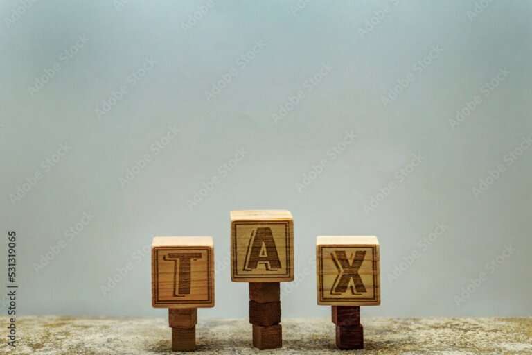 税金のイメージでブロックを積み上げた頂上にTAXのアルファベットのウッドキューブ